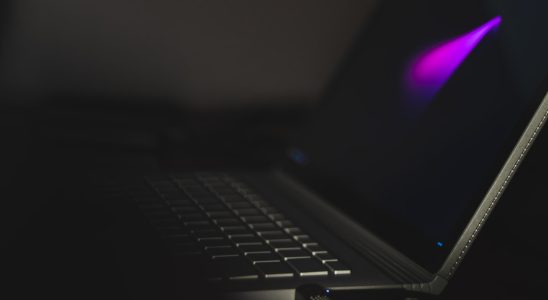 Close-up of a laptop keyboard with a faint purple glow on the screen in a dim environment.