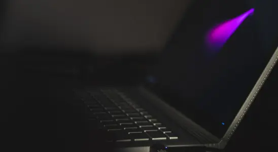 Close-up of a laptop keyboard with a faint purple glow on the screen in a dim environment.